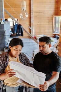 Two professionals reviewing construction plans indoors during the day. Two professionals reviewing construction plans indoors during the day.